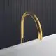 Freistehender Wanneneinlauf in Brushed Gold von Ideal Standard, mit geschwungener Form und minimalistischer Gestaltung, vor einer dunklen Fliesenwand.